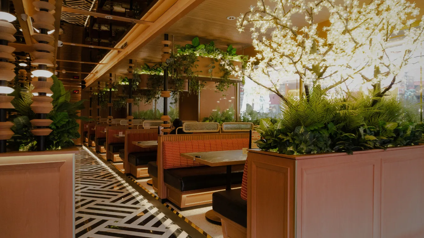 Restaurant interior with planted booth seating and an illuminated floral feature